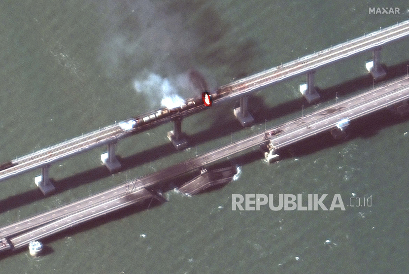 Gambar satelit yang disediakan oleh Maxar Technologies ini menunjukkan kerusakan pada Jembatan Kerch, yang menghubungkan Semenanjung Krimea, kanan atas, dengan Rusia, kiri bawah, melintasi selat antara Laut Hitam dan Laut Azov, dan gerbong terbakar, kanan atas , pada hari Sabtu, 8 Oktober 2022. Utara mengarah ke kanan.