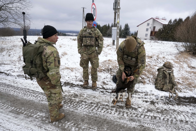 Seorang tentara AS bermain dengan seekor anjing di sebuah kamp militer di Arlamow, Polandia tenggara, dekat perbatasan dengan Ukraina, pada Senin, 28 Februari 2022.  Invasi Rusia ke Ukraina membuat hewan-hewan liar dari suaka di timur Kiec ikut mengungsi ke Polandia.