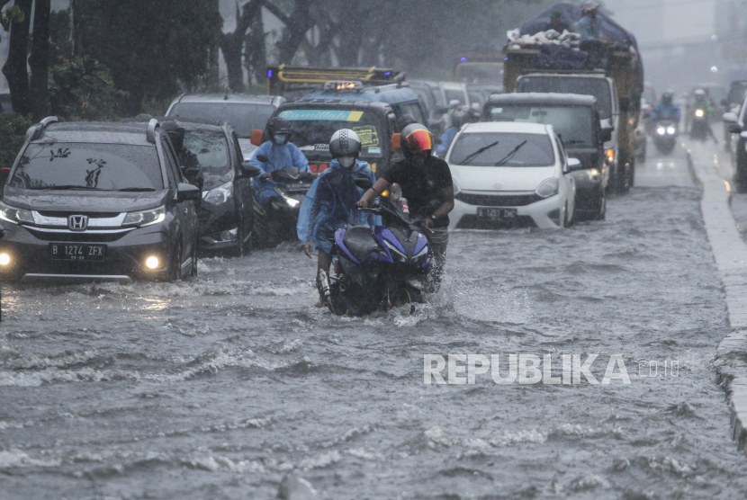 Pengendara mendorong sepeda motor yang mogok saat melintasi genangan air di Jalan Margonda Raya, Kota Depok, Jawa Barat, Kamis (5/8/2021).