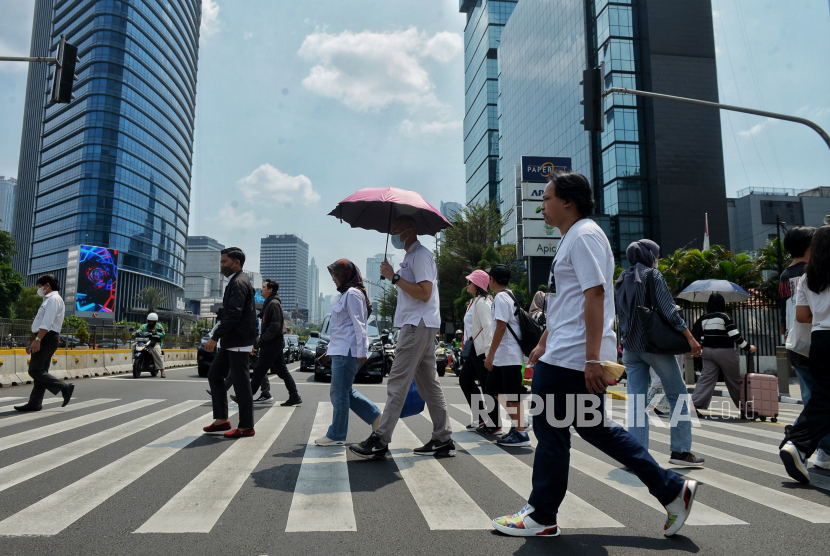 Perkeja melindungi tubuh dari terik matahari menggunakan payung saat berjalan di kawasan Sudirman, Jakarta.