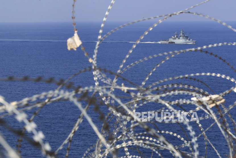  Sebuah kapal Angkatan Laut UNIFIL terlihat melalui patroli kawat berduri di Laut Mediterania, di sebelah pos PBB di sepanjang perbatasan yang dikenal sebagai Ras Naqoura, tempat delegasi Lebanon dan Israel akan bertemu, di lepas kota selatan Naqoura, Lebanon, Kamis, 10 Oktober. 27 Oktober 2022. Lebanon menandatangani dan mengirimkan salinan kesepakatan perbatasan laut yang dimediasi AS dengan Israel pada hari Kamis kepada mediator AS, berharap untuk segera mulai mengeksplorasi gas di blok maritim selatannya untuk membawa stabilitas ekonomi ke negara yang dilanda krisis.