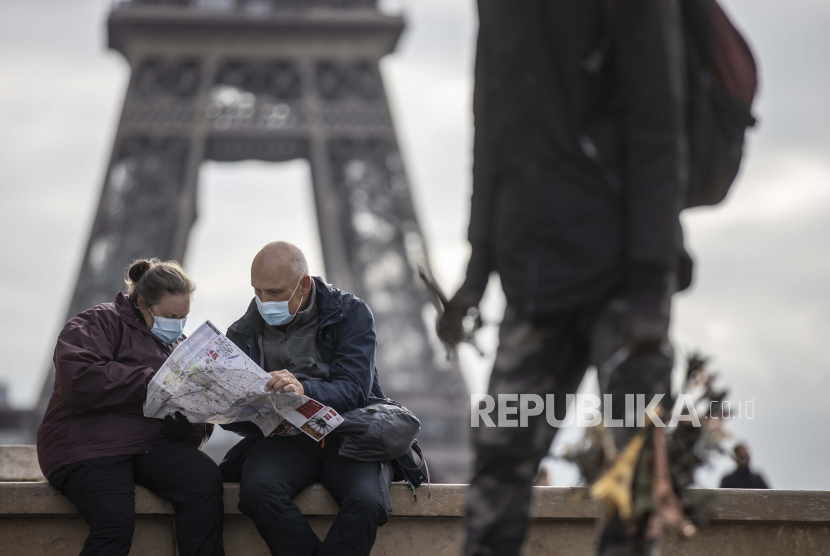Pejalan kaki memakai masker pelindung saat mereka melihat peta di dekat Menara Eiffel di Paris, Prancis. Prancis cabut syarat tes Covid-19 demi memulihkan kembali ekonomi pascapandemi. Ilustrasi.