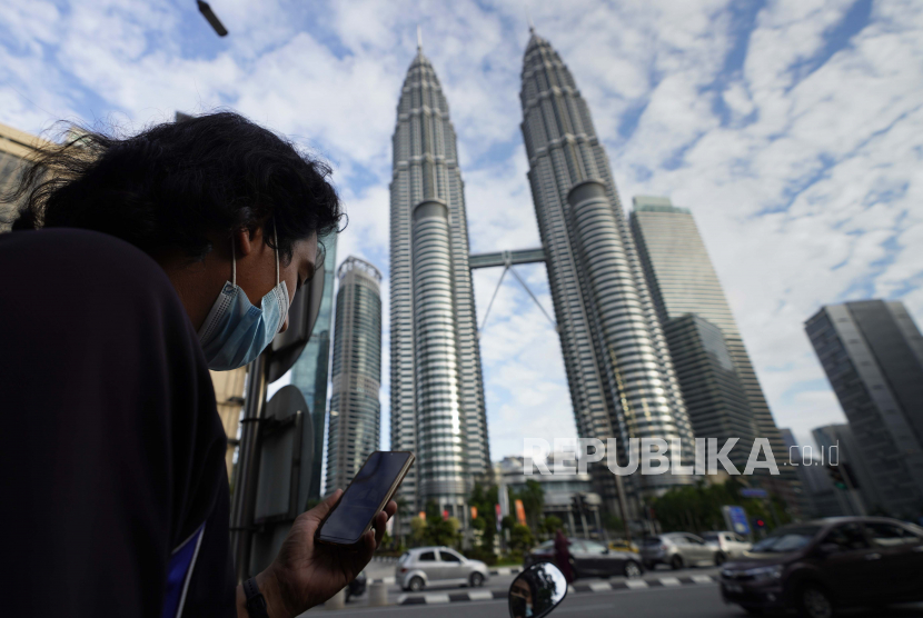 Seorang pria yang memakai masker wajah mendengarkan siaran langsung di depan Menara Kembar di pusat kota Kuala Lumpur, Malaysia, Senin, 11 Januari 2021. Perdana Menteri Muhyiddin Yassin mengubah strategi penanganan pandemi dengan tidak memberlakukan PKP di seluruh bagian Malaysia.