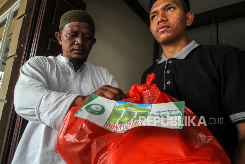 Relawan Majelis Taklim Raudhatul Jannah  Maulana (kiri) menyerahkan bantuan sembako kepada warga di Lhokseumawe, Aceh, Jumat (27/3/2020). Bantuan Sembilan bahan pokok itu untuk membantu para keluarga rawan miskin baru (tidak berpenghasilan) yang terdampak penyebaran virus corona (COVID-19)
