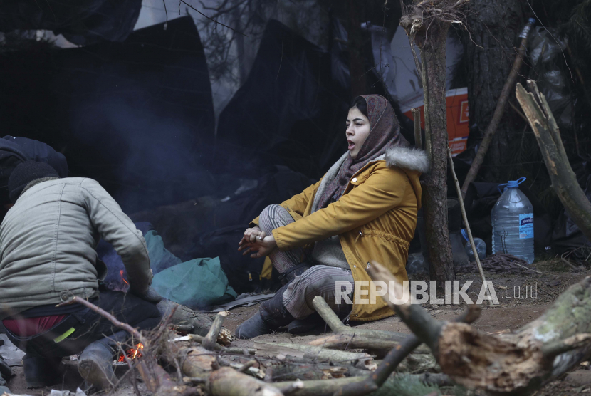 Seorang wanita muda menghangatkan dirinya di api ketika migran lain berkumpul di perbatasan Belarus-Polandia dekat Grodno, Belarus, 14 November 2021. Para migran terjebak di perbatasan Polandia-Belarusia dalam kondisi lapar dan lelah.