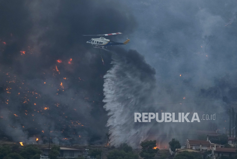 Helikopter pemadam kebakaran membuang air saat api mendekati rumah di Kalamaki dekat Agioi Theodori sekitar 60 kilometer sebelah barat Athena, Yunani, Selasa, (18/7/2023).