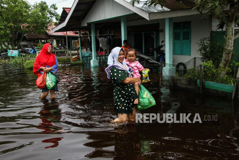 Warga berjalan melewati banjir di Jalan Pelatuk IV, Palangka Raya, Kalimantan Tengah, Ahad (10/3/2024). Curah hujan yang tinggi serta meluapnya Sungai Kahayan, Rungan, dan Sebangau mengakibatkan 16 kelurahan di empat kecamatan Kota Palangka Raya terendam banjir. 