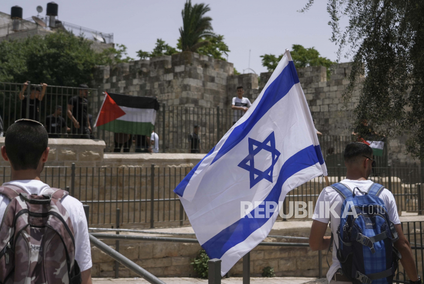 Warga Palestina dan Israel mengibarkan bendera nasional mereka di luar Kota Tua Yerusalem saat warga Israel memperingati Hari Yerusalem, hari libur Israel yang merayakan penaklukan Kota Tua selama perang Timur Tengah 1967. Ahad, 29 Mei 2022. 