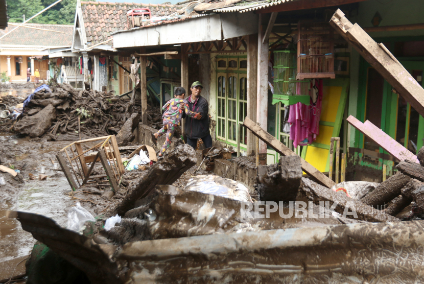 Warga menggendong seorang anak melintasi material lumpur yang merendam rumahnya pascabanjir bandang di Desa Kalisat, Ijen, Bondowoso, Jawa Timur, Senin (13/2/2023). Sebanyak 49 rumah warga di Desa Kalisat dan 29 rumah di Desa Sempol akan direlokasikan ke tempat yang lebih aman karena lokasinya tersebut rawan terjadi banjir. ANTARA FOTO/Budi Candra Setya/rwa.