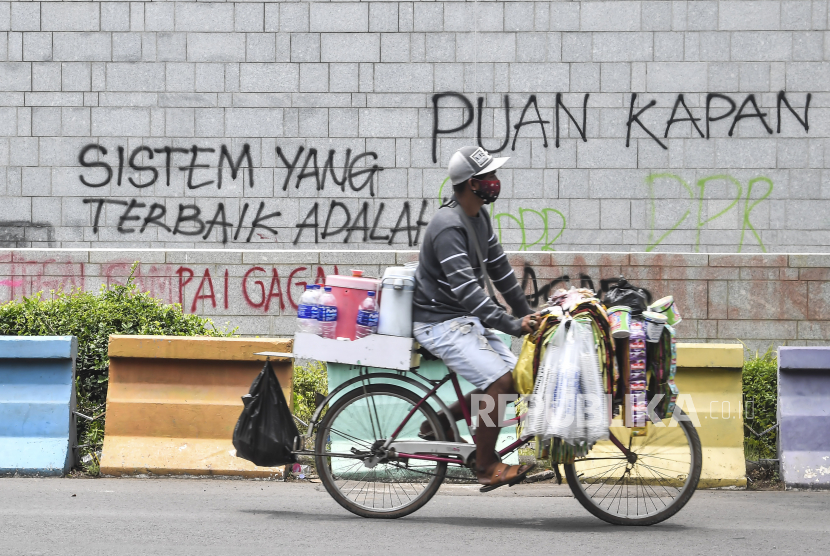 Penjual minuman mengayuh sepedanya di depan tembok yang dicoret-coret oleh orang tidak bertanggungjawab saat aksi Tolak UU Cipta Kerja di depan Kedutaan Amerika Serikat, Jakarta, Rabu (14/10/2020). 