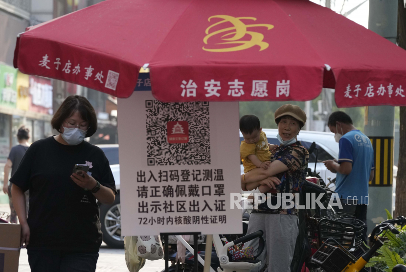 Warga mengenakan masker melewati dekat kode QR yang digunakan untuk memindai status kode kesehatan, Senin, 20 Juni 2022, di Beijing.