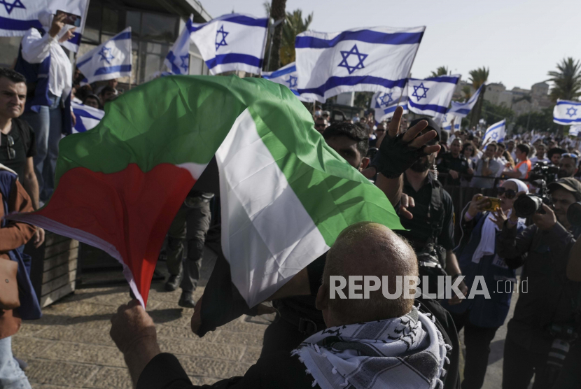 Seorang pria Palestina mengibarkan bendera nasionalnya saat warga Israel memperingati Hari Yerusalem, hari libur Israel merayakan penaklukan Kota Tua selama perang Timur Tengah 1967, di luar Kota Tua Yerusalem, Ahad, 29 Mei 2022.