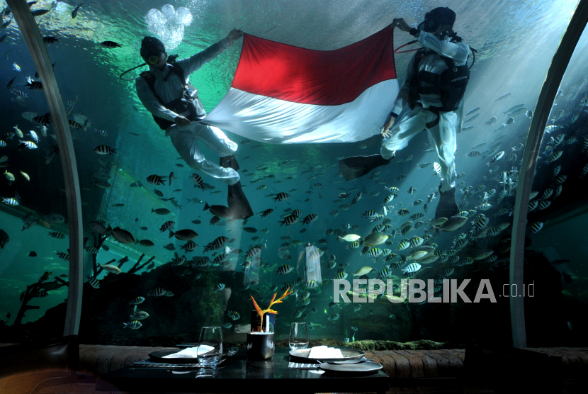 Penyelam mengibarkan bendera merah putih di dalam akuarium Koral Restaurant, The Apurva Kempinski Bali, Badung, Bali, Selasa (17/8/2021). Pengibaran bendera di bawah air oleh penyelam yang mengenakan seragam petugas upacara tersebut dilakukan untuk memeriahkan peringatan HUT ke-76 Kemerdekaan RI. 
