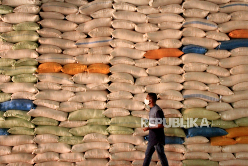 Seorang pria berjalan di dekat tumpukan karung berisi beras di gudang Bulog wilayah NTT di Kupang, NTT, Senin (18/5). Bulog mencatat peningkatan tajam penjualan pangan lewat toko daring.