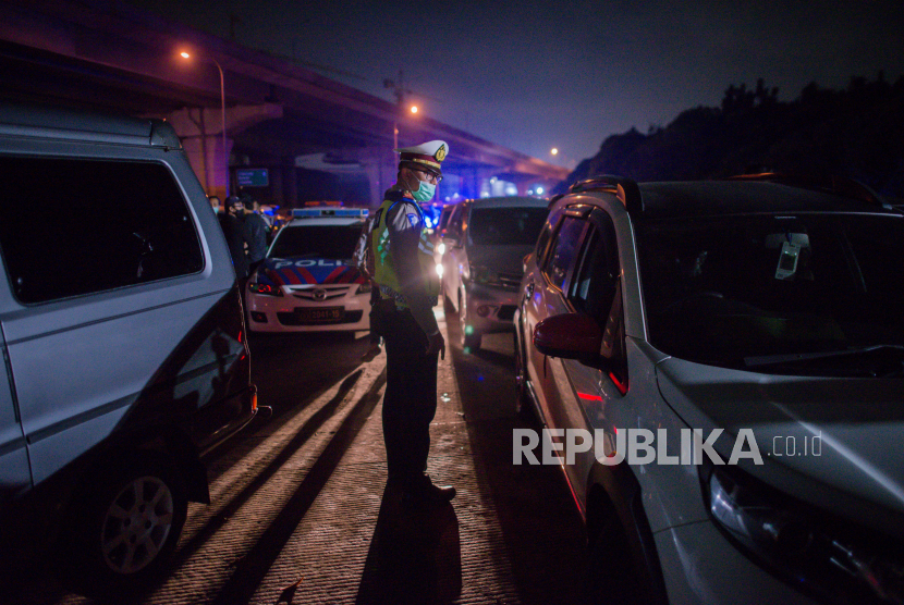 Petugas kepolisian mengarahkan kendaraan pribadi untuk keluar di Gerbang Tol Cikarang Barat, Bekasi, Jawa Barat, Sabtu (23/5) dini hari. Sekitar 200 pemudik yang menggunakan jasa travel tanpa izin beserta kendaraan pribadi terkena razia penyekatan dan akan dikembalikan ke Jakarta