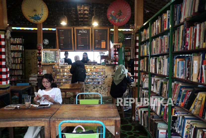 Pengunjung menikmati minuman dengan membaca buku di kedai kopi, (ilustrasi).