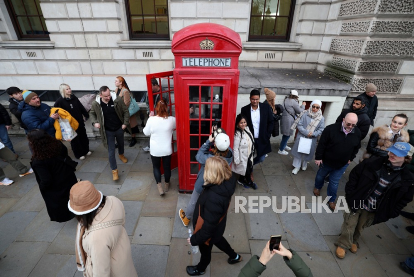 Turis asing berkumpul di sekitar kotak telepon umum berwarna merah di Westminster, London, Inggris, (29/1/2023).