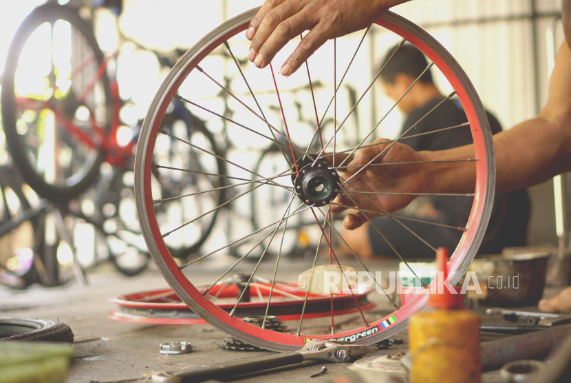 Mekanik sepeda memasang jari-jari roda sepeda mini lipat di sebuah bengkel sepeda rumahan. Ilustrasi