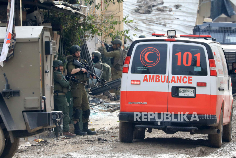 Tentara bersenjata Israel berjaga-jaga setelah menggeledah ambulans Masyarakat Bulan Sabit Merah Palestina saat mereka memblokir akses ke jalan di kota Tulkarem,Rabu, (17/1/2024).