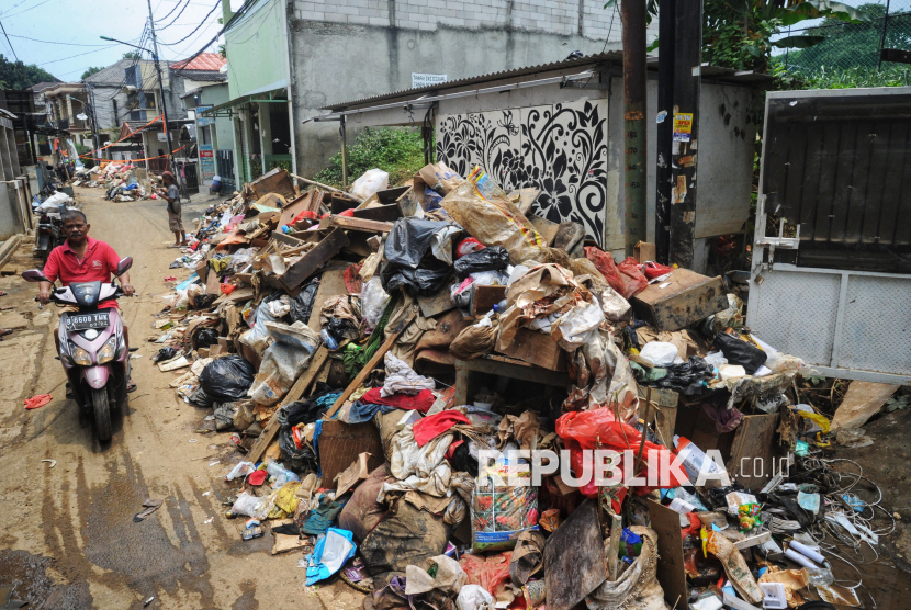 Warga melintas disamping tumpukan sampah sisa banjir di kawasan RW 07, Cililitan, Jakarta, Ahad (9/3/2025). 