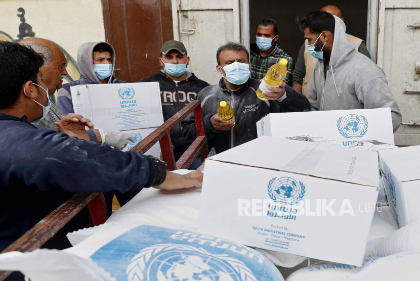 Pekerja Palestina memuat persediaan makanan yang didistribusikan oleh Badan Bantuan dan Pekerjaan PBB (UNRWA) 