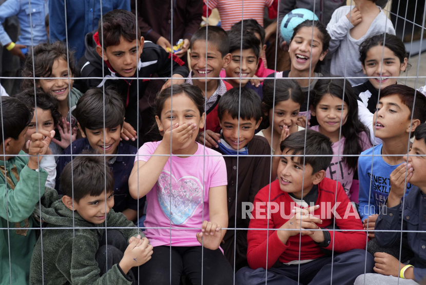 Masjid York Ajak Donasi Mainan untuk Pengungsi Afghanistan. Anak-anak Afghanistan yang baru dievakuasi tertawa di balik pagar sementara seorang tentara AS bermain gitar di Pangkalan Udara AS Ramstein, Jerman, Selasa, 24 Agustus 2021.
