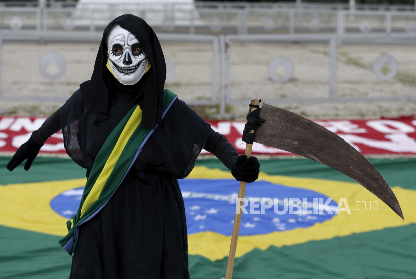 Seorang demonstran berpakaian seperti kematian dan mengenakan selempang kepresidenan bergabung dengan protes terhadap tanggapan Presiden Brasil Jair Bolsonaro terhadap pandemi COVID-19, di luar istana kepresidenan Planalto, di Brasilia, Brasil, Minggu, 17 Januari 2021.