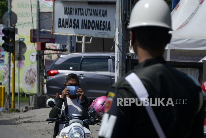 Seorang pengendara menggunakan maskernya sebelum melewati pemeriksaan petugas saat uji coba penerapan Pembatasan Sosial Berskala Besar (PSBB) di Makassar, Sulawesi Selatan, Selasa (21/4/2020). Pemerintah kota Makassar melakukan uji coba penerapan PSBB selama tiga hari agar penerapan PSBB yang akan dilaksanakan pada (24/4/2020) dapat berjalan efektif  dalam percepatan penanganan COVID-19