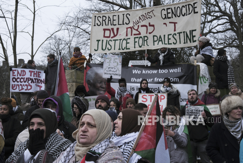 Para pengunjuk rasa memegang spanduk dan mengibarkan bendera Palestina selama demonstrasi di luar Mahkamah Internasional di Den Haag, Belanda, Kamis, (11/1/2024).
