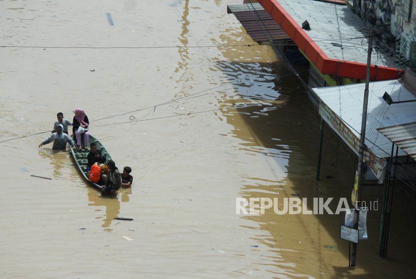 Warga menaiki perahu untuk melintasi jalang yang tergenang banjir.