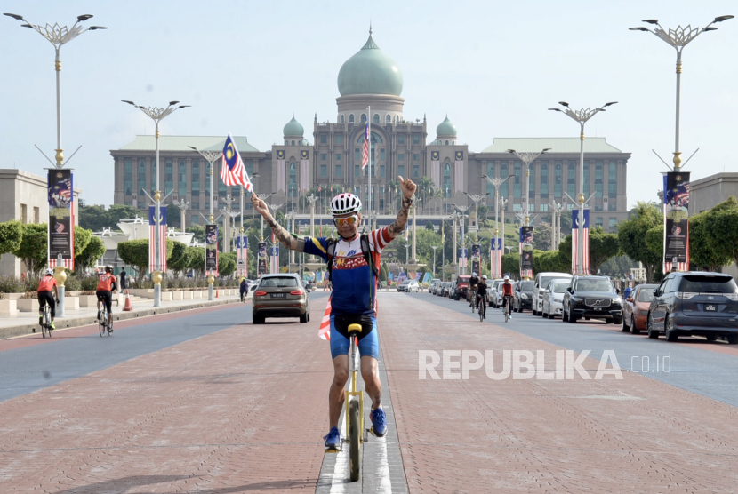 Seorang pesepeda roda satu membawa bendera jalur gemilang saat merayakan Hari Ulang Tahun (HUT) Kemerdekaan atau Hari Kebangsaan ke-63 Malaysia dengan latar belakang Kantor Perdana Menteri Malaysia di Putrajaya, Malaysia, Senin (31/8/2020). Malaysia merayakan Hari Kemerdekaan secara sederhana pada masa pandemi COVID-19. 