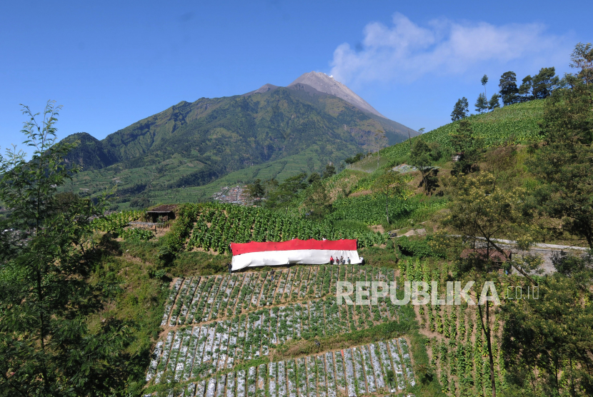 Sejumlah warga membentangkan bendera merah putih dengan berlatar belakang Gunung Merapi di lahan pertanian kaki Gunung Merbabu, Selo Tengah, Selo, Boyolali, Jawa Tengah, Selasa (17/8/2021). 