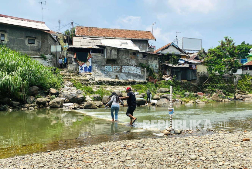 Warga menyeberangi aliran Sungai Ciliwung melalui jembatan darurat. Iwan menjadi pahlawan warga karena membuat jembatan darurat di Ciliwung dengan karung