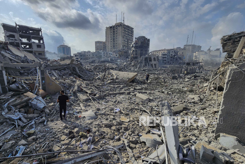 Warga Palestina berjalan melewati puing-puing bangunan yang hancur akibat serangan udara Israel di Kota Gaza pada Selasa, 10 Oktober 2023.