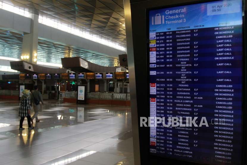 Penumpang melintas disamping monitor jadwal penerbangan yang memperlihatkan pengumuman pembatalan penerbangan di Terminal 3 Bandara Soekarno Hatta, Tangerang, Banten.