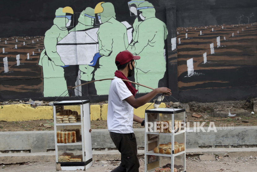  Seorang penjual roti melewati mural bertema virus corona di Jakarta, Indonesia. Polri berencana menggandeng preman pasar untuk menegakkan pelanggaran protokol kesehatan Covid-19.