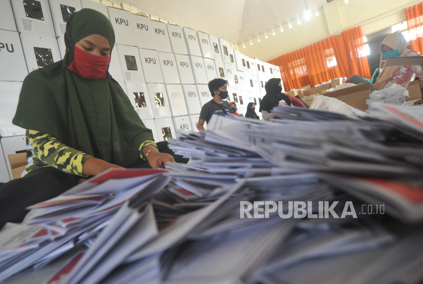 Pekerja bermasker melakukan pelipatan surat suara di gudang kantor KPU.