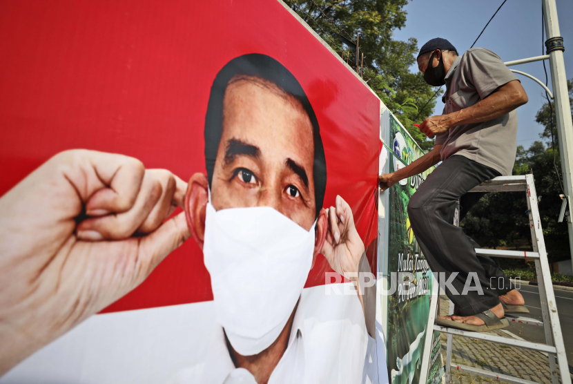 [Ilustrasi] Seorang pekerja duduk di tangga sembari memasang spanduk bertema coronavirus awareness dengan gambar Presiden Indonesia Joko Widodo memakai masker, di Jakarta.