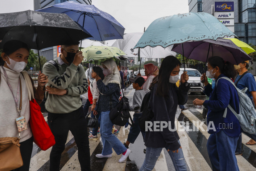 Orang-orang memegang payung di bawah hujan, melintasi jalan yang sibuk di Jakarta. (ilustrasi)