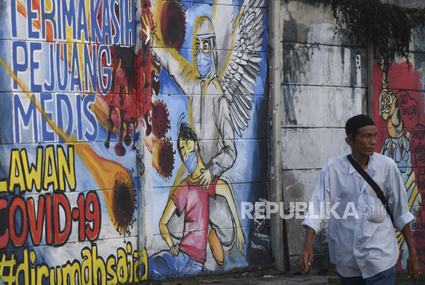Seorang warga melintasi mural ajakan melawan Covid-19 di Depok, Jawa Barat, Selasa (14/4/2020). Pemprov Jawa Barat akan memulai pembatasan sosial skala besar (PSBB) di Bogor, Depok, Bekasi sebagai kota penyangga Ibu Kota pada Rabu (15/4) dengan menyiapkan anggaran Rp4 triliun sebagai jaring pengaman sosial