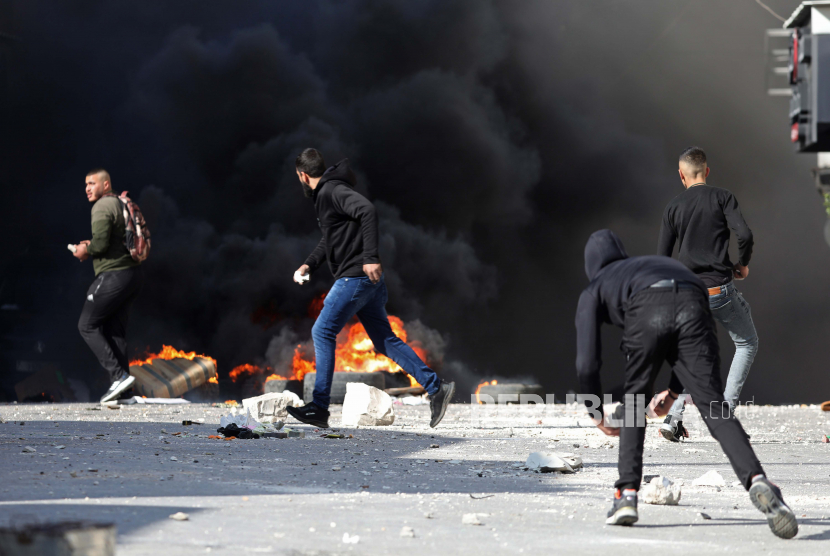 Warga Palestina berlarian di tengah asap selama bentrokan setelah serangan militer Israel di kota Nablus, Tepi Barat utara, 30 Desember 2022. Sepuluh warga Palestina terluka dalam bentrokan itu menurut sumber medis Palestina.