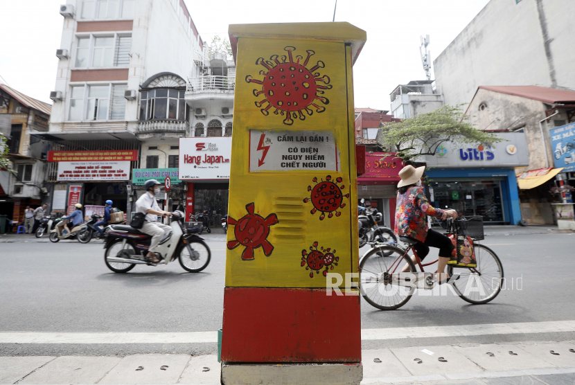 Orang-orang melewati kotak listrik yang dicat dengan tema COVID-19 di Hanoi, Vietnam, 07 Juni 2021.