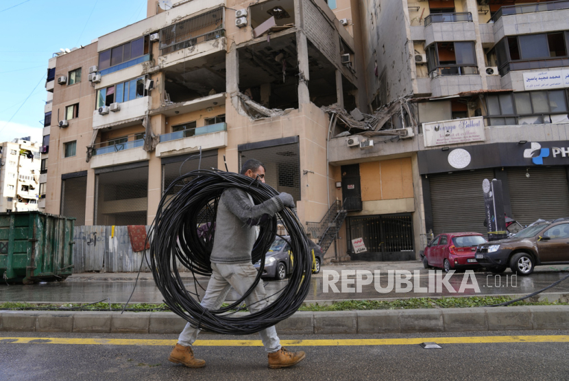 Pekerja membawa kabel listrik lewat di depan sebuah gedung apartemen tempat serangan Israel di pinggiran selatan Beirut yang merupakan kubu Hizbullah, Lebanon, Rabu, (3/1/2024).