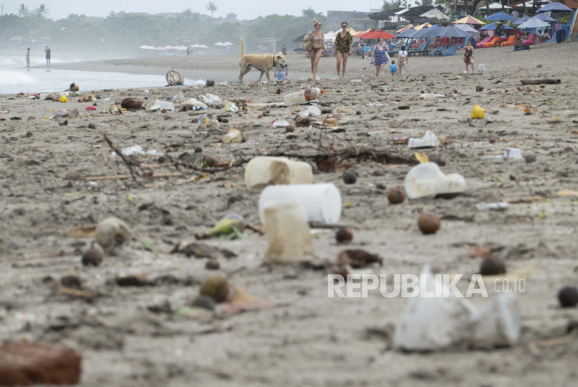 Turis berjalan di sepanjang pantai yang tertutup puing-puing dan sampah plastik di Canggu, Bali.