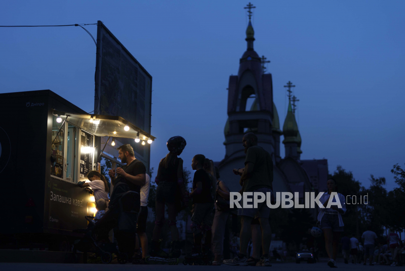 Pelanggan mengantre di kios kopi di taman saat gereja ortodoks Ukraina berdiri di latar belakang di Dnipro, Ukraina, Rabu, 17 Agustus 2022. Badan Keamanan Ukraina mengatakan 10 pemuka agama di gereja pro-Rusia di Ukraina mendapat sanksi.