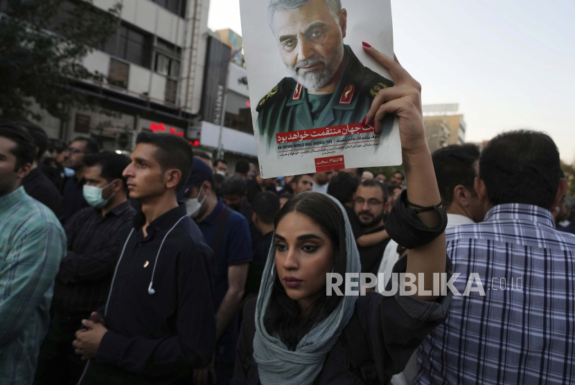 Seorang demonstran pro-pemerintah Iran mengangkat poster mendiang Pengawal Revolusi Jenderal Qassem Soleimani, yang tewas di Irak dalam serangan pesawat tak berawak AS pada tahun 2020, selama rapat umum yang mengutuk protes anti-pemerintah baru-baru ini atas kematian Mahsa Amini, seorang demonstran pro-pemerintah Iran. Wanita berusia 22 tahun itu ditahan oleh polisi moral bangsa, di Teheran, Iran, Minggu, 25 September 2022. Ulama Senior Iran Serukan Tindakan Keras Terhadap Demonstran Mahsa Amini