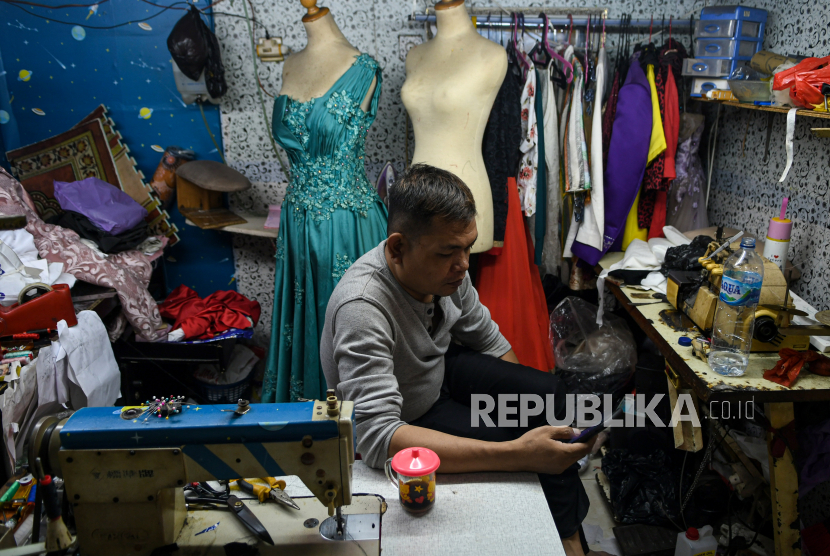 Seorang penjahit mengoperasikan ponselnya pada lapaknya di Metro Atom, Pasar Baru, Jakarta, Minggu (3/5). Sebanyak 8,33 juta UMKM debitur KUR dengan outstanding Rp165 triliun diberi keringanan kredit.