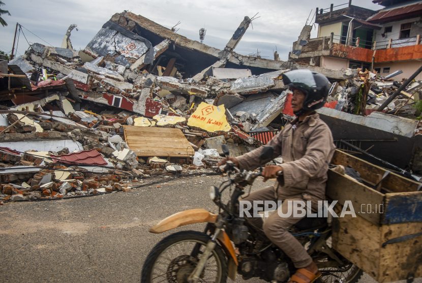  Seorang pria mengendarai sepeda motornya melewati rumah-rumah yang ambruk setelah gempa bumi di Mamuju, Sulawesi Barat, Indonesia, 17 Januari 2021. Sedikitnya 56 orang tewas dan ratusan lainnya luka-luka setelah gempa berkekuatan 6,2 skala Richter melanda pulau Sulawesi pada 15 Januari.