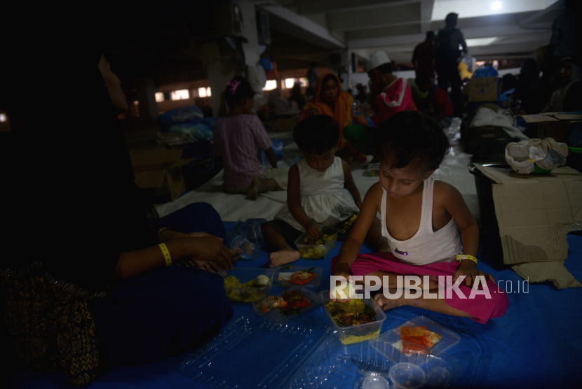 Sejumlah imigran etnis Rohingya bersama anaknya menyantap makanan bantuan dari kelompok masyarakat di penampungan sementara gedung  Balai Meuseuraya Aceh (BMA), Banda Aceh, Aceh, Ahad (31/12/2023). Kelompok masyarakat di Aceh menyalurkan bantuan kemanusian berupa makanan dari sumbangan warga kepada sebanyak 137 pengungsi imigran etnis Rohingya terdiri dari laki-laki, perempuan dan anak anak yang masih menempati ruangan parkir gedung BMA. 
