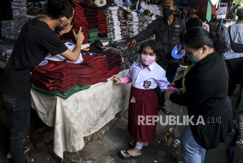 Calon pembeli mengenakan pakaian seragam sekolah kepada anaknya di Pasar Jatinegara, Jakarta, Ahad (5/7/2020).  Pemerintah Provinsi DKI Jakarta pastikan tahun ajaran baru 2020-2021 yang dimulai pada 13 Juli 2020 masih dilakukan secara daring atau belajar dari rumah.